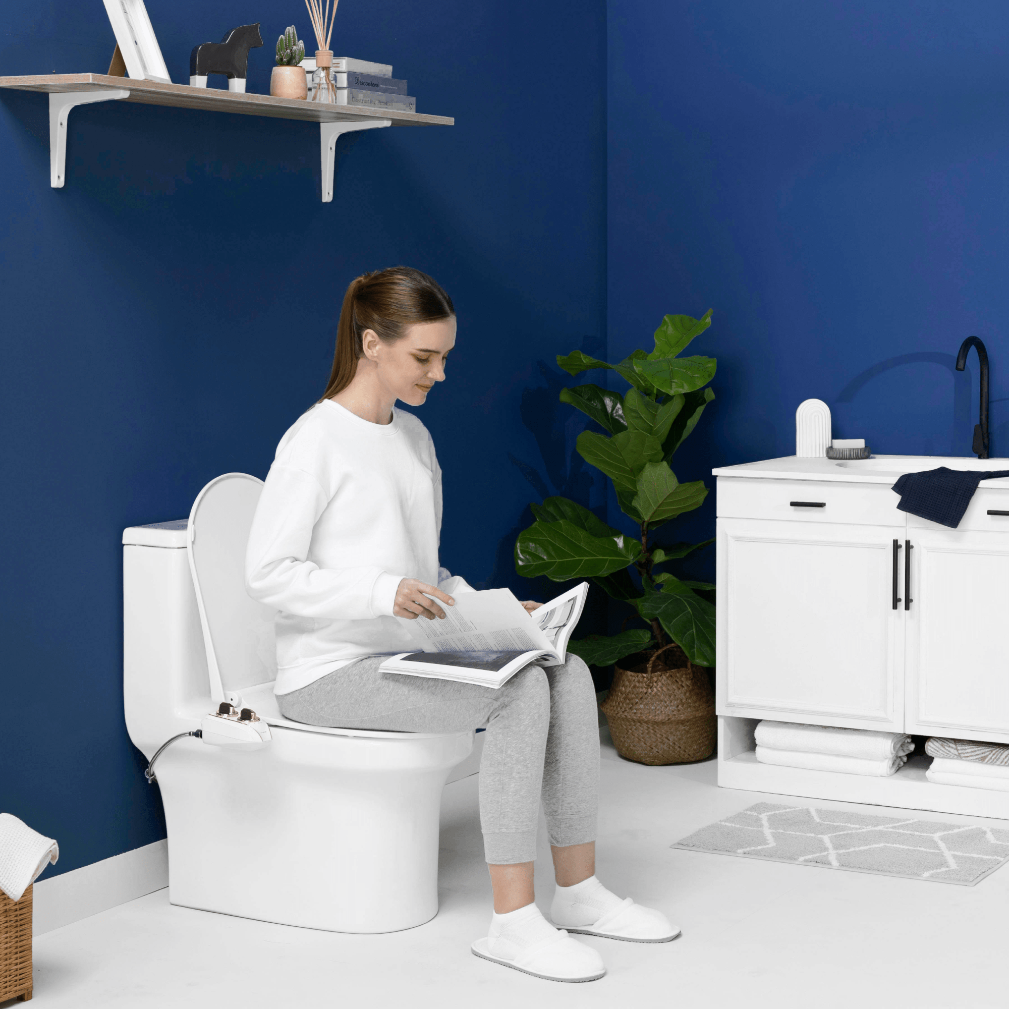 NEO 120 Plus Rose Gold installed, with a person sitting on the toilet reading, in a modern blue bathroom