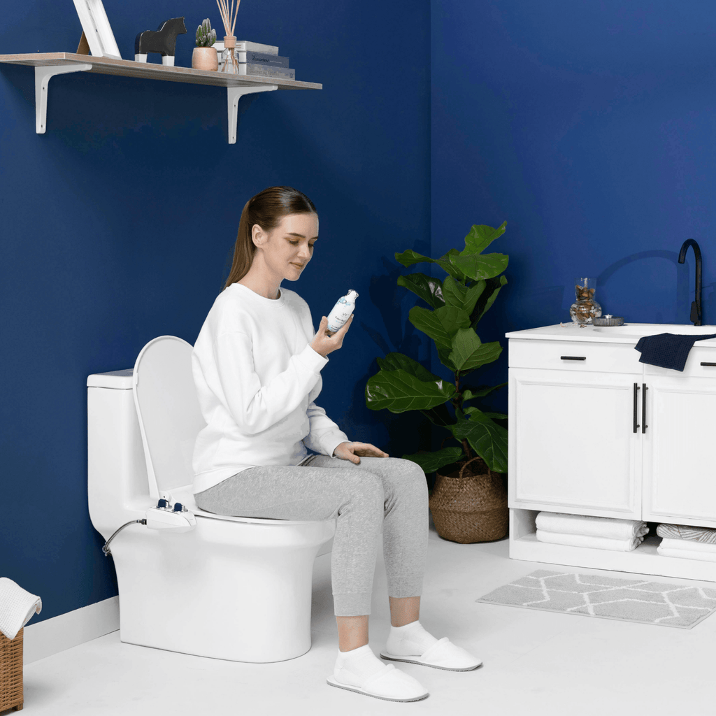 NEO 185 Plus Chrome installed, with a person sitting on the toilet holding a Whift bottle, in a modern blue bathroom