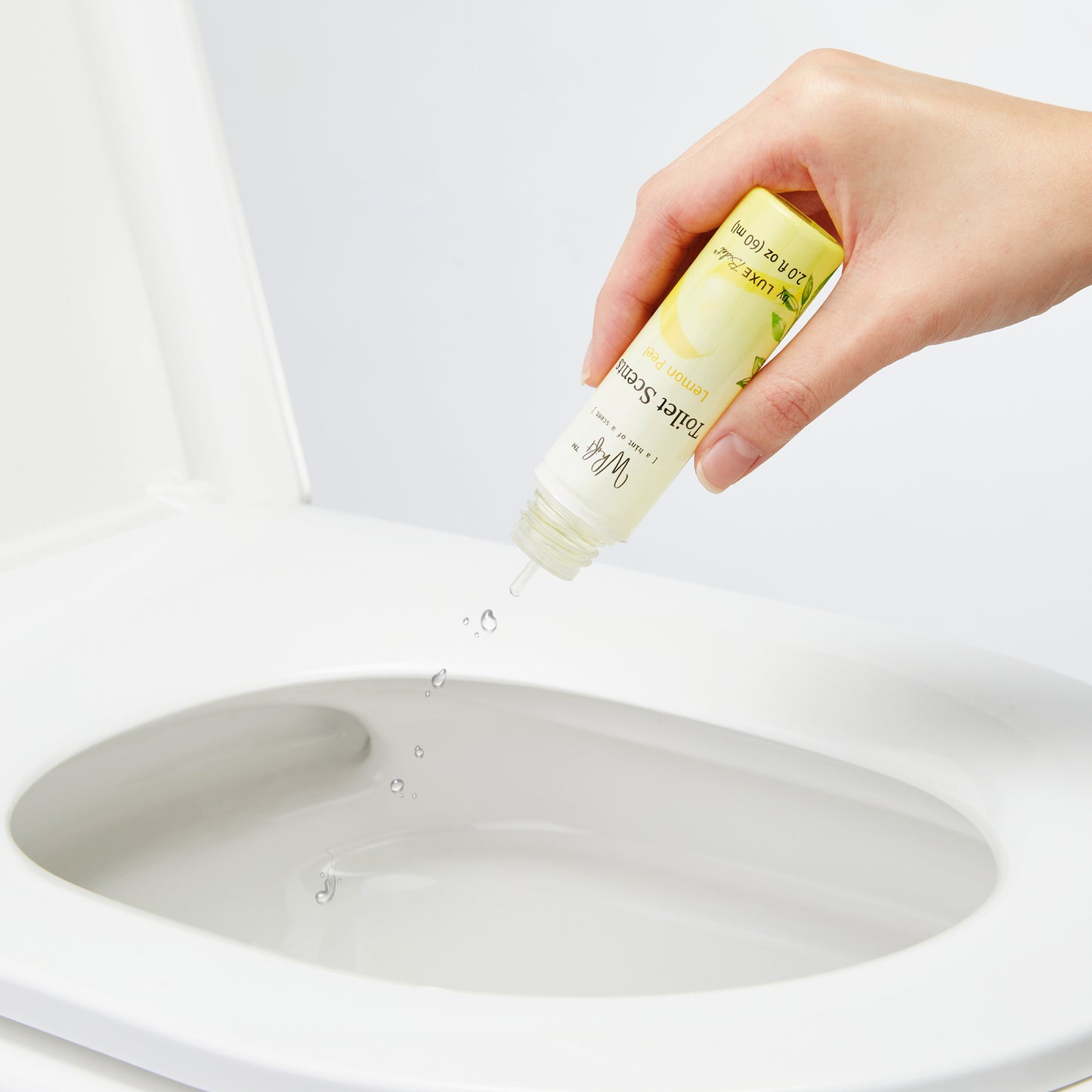 Hand squeezing drops of Lemon Peel Whift Drops into the toilet