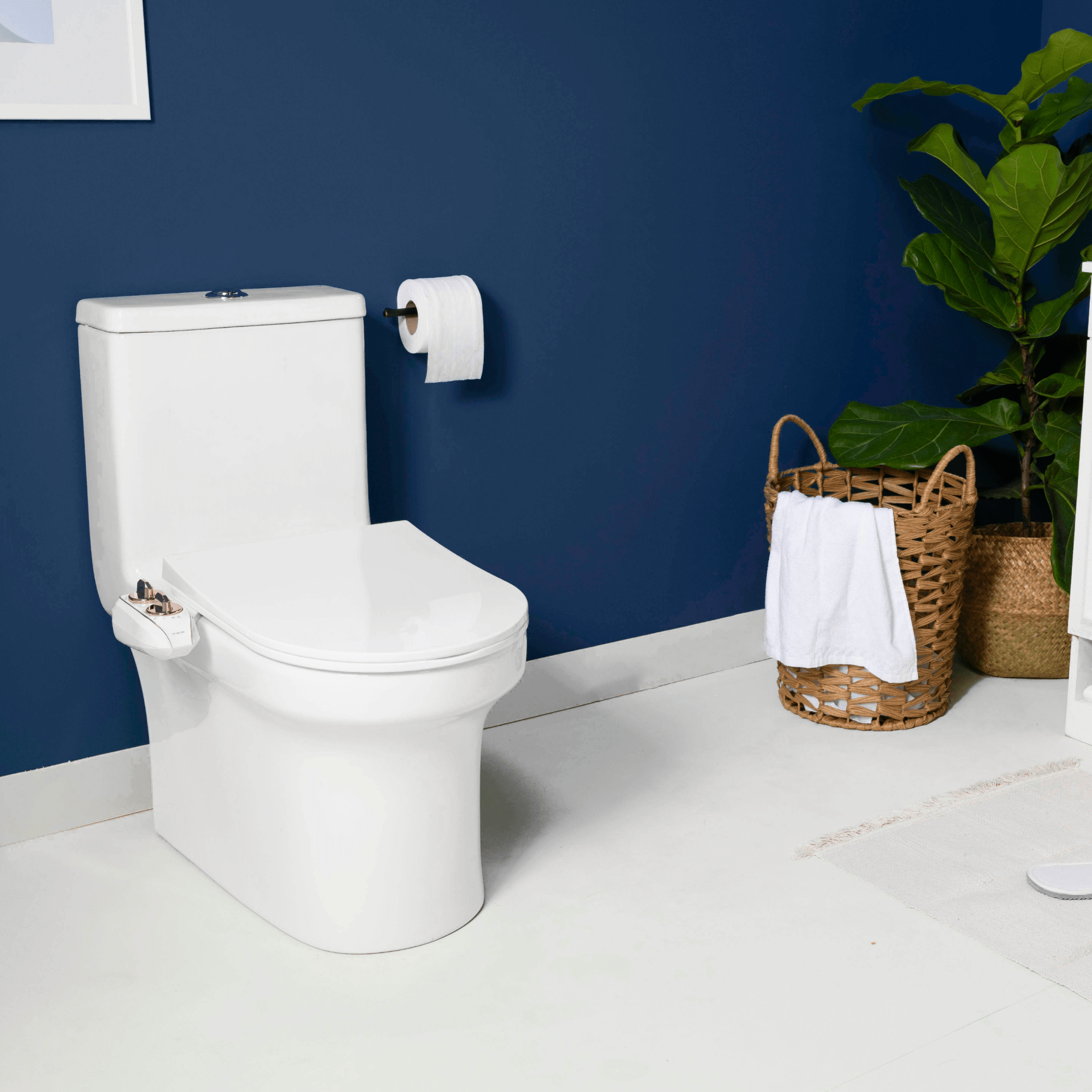 NEO 185 Plus Rose Gold installed on a toilet, in a modern blue bathroom with a plant and basket of towels