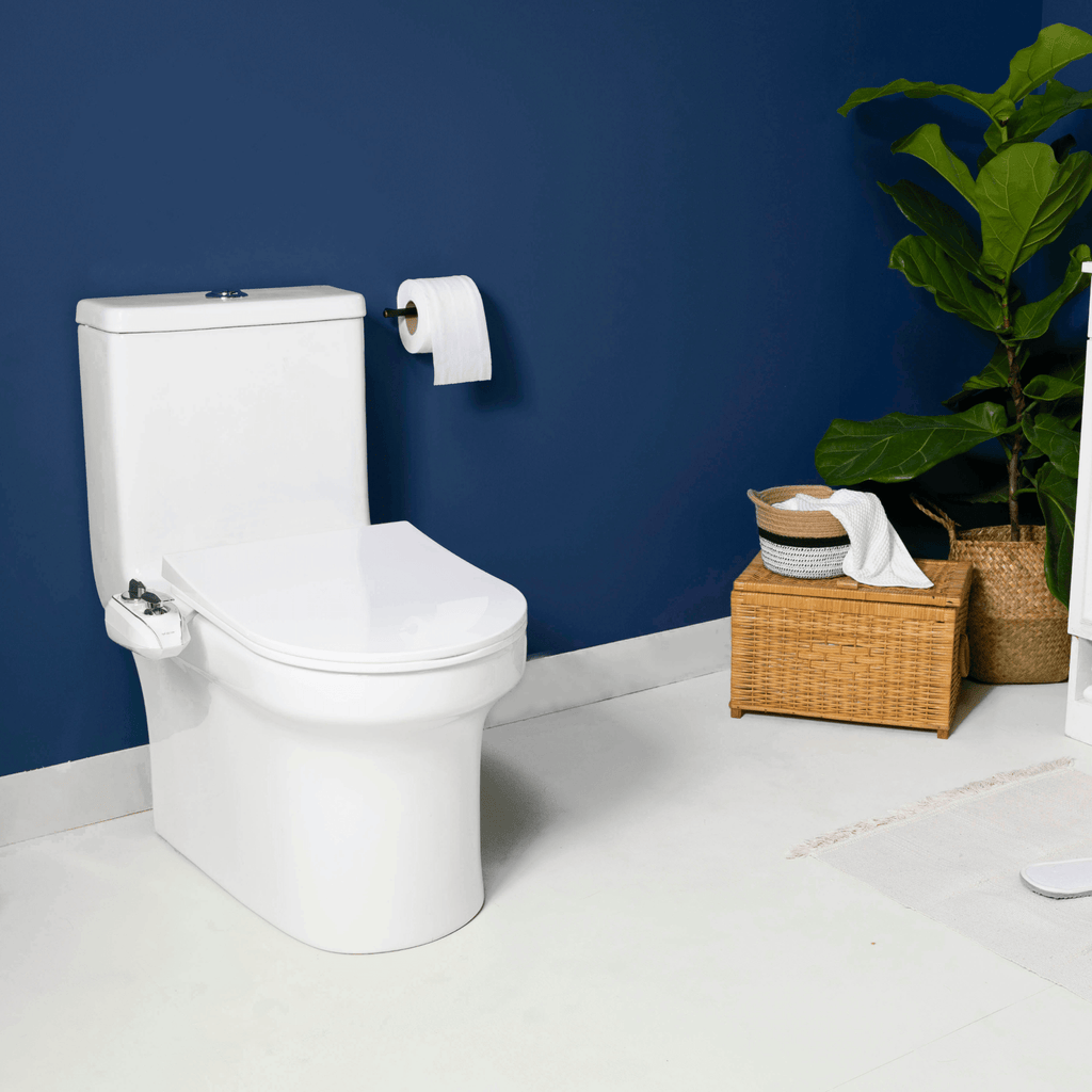 NEO 320 Plus Chrome installed on a toilet, in a modern blue bathroom with a plant and basket of towels