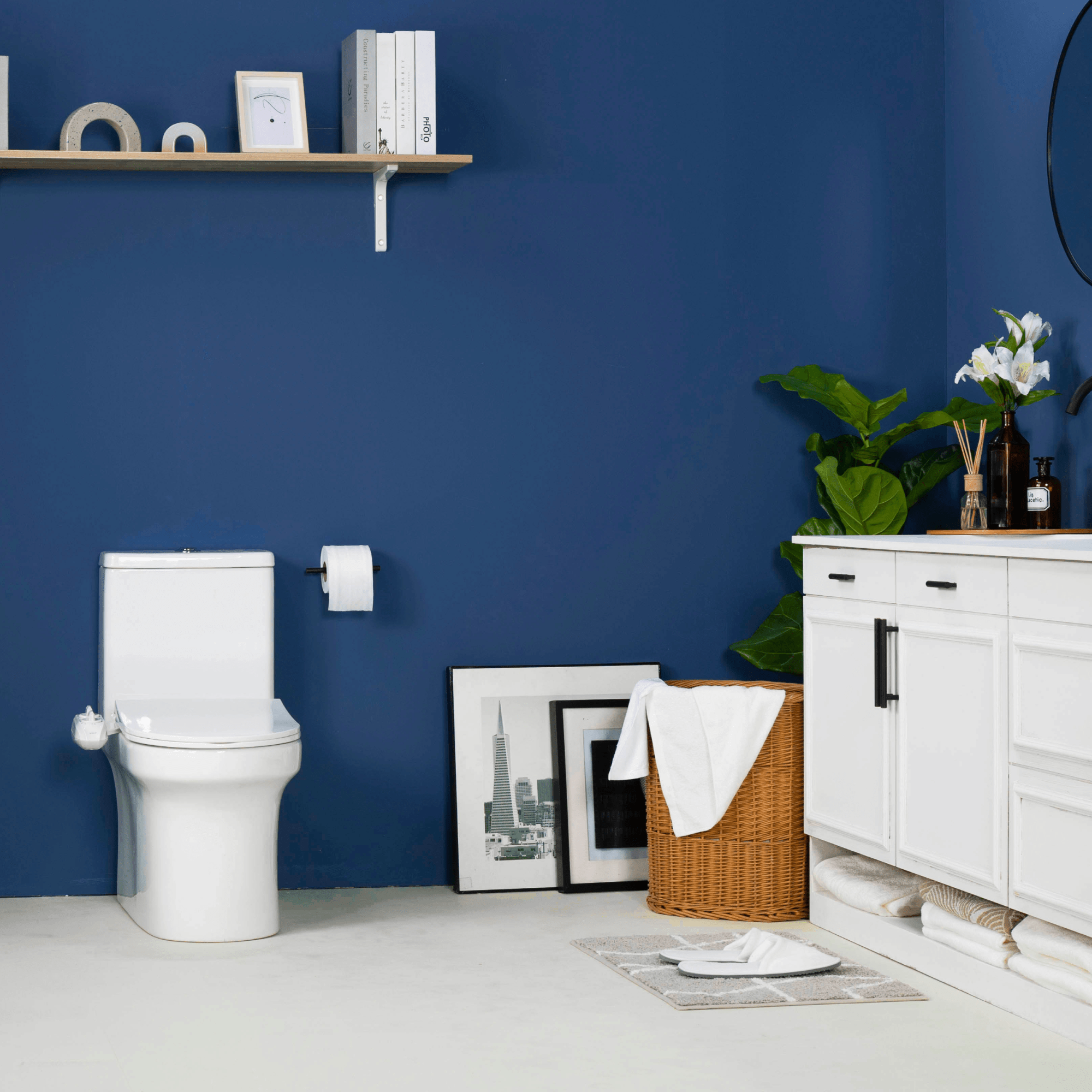 NEO 120 Plus White installed on a toilet, in a modern blue bathroom with a plant, painting, and basket of towels