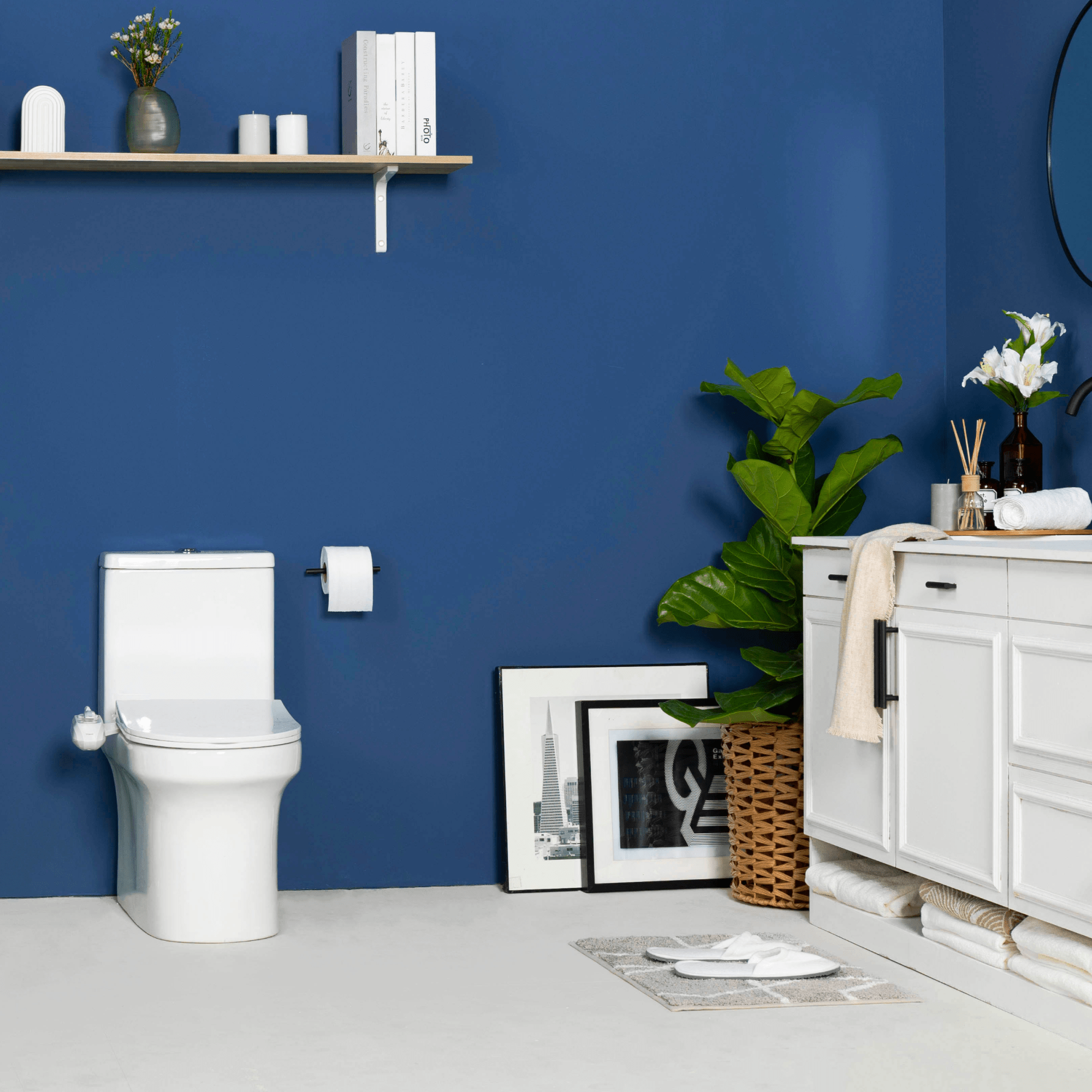 NEO 320 Plus White installed on a toilet, in a modern blue bathroom with a cabinet, paintings, and a plant