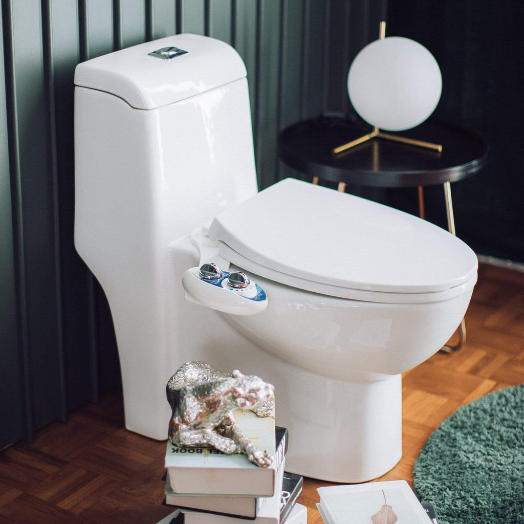 NEO 120 Blue installed on a toilet in a modern green wooden bathroom with a table, mirror, and stack of books